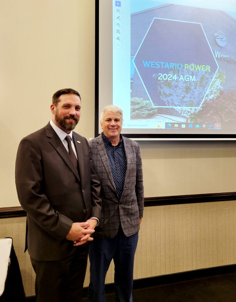 Board Chair Charbonneau and Vice-Chair Peabody standing in front of an image presenting the 2024 AGM on a projector screen